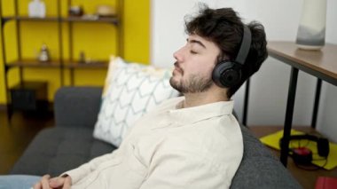 Genç İspanyol adam evdeki kanepede oturmuş müzik dinliyor.