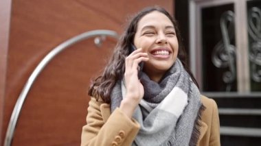 Genç, güzel İspanyol bir kadın akıllı telefondan konuşuyor. Sokakta gülümsüyor.