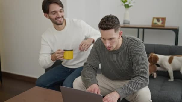 Двое Мужчин Используют Ноутбук Пьют Кофе Целуются Дома — стоковое видео