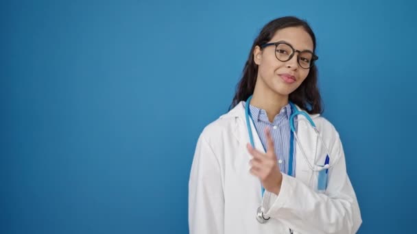 若いです美しいですヒスパニック女性医師笑顔上の側面を指して隔離された青の背景 — ストック動画