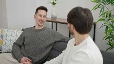 İki erkek kanepede oturup birbirlerine sarılıyorlar.