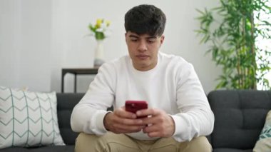 Evdeki kanepede oturmuş akıllı telefon kullanan genç bir İspanyol.