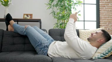 Evdeki kanepede uzanmış akıllı telefon kullanan genç bir İspanyol.