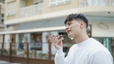 Latin kökenli genç adam kahve dükkanının terasında akıllı telefonuyla sesli mesaj yolluyor.