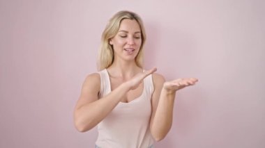 Kendine güvenen genç sarışın bir kadın. Soyutlanmış pembe arka planda para harcıyor.