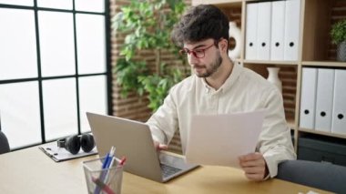 Young hispanic man business worker using laptop reading document at office