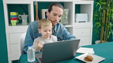 Baba ve oğul yemek odasında çalışıyor ve çocuğa bakıyor.