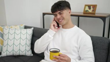Genç İspanyol adam akıllı telefonda konuşuyor. Evde kahve içiyor.
