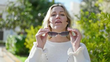 Parkta güneş gözlüğü takan, kendine güvenen genç sarışın kadın.