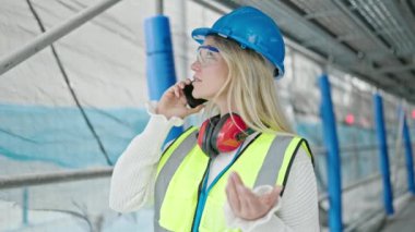 Sarışın genç bir mimar sokakta akıllı telefondan konuşuyor.
