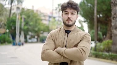 Ciddi bir ifade ve kollarını kavuşturarak parkta dikilen İspanyol genç bir adam.
