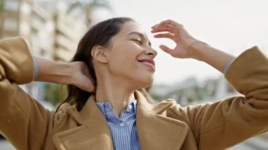 Young beautiful hispanic woman smiling confident combing hair with hands at street