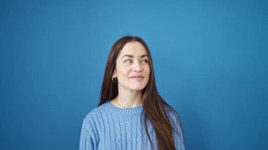 Şaşırtıcı bir ifadeyle duran genç beyaz kadın, izole edilmiş mavi arka plana bakıyor.