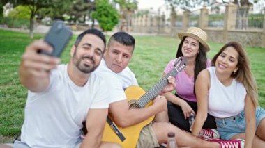 Bir grup insan parkta piknik yaparken akıllı telefondan selfie çekiyor.