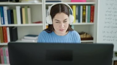Kütüphane üniversitesinde bilgisayar ve kulaklık kullanan beyaz bir kız öğrenci.