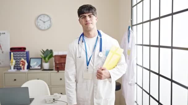 若いヒスパニック系の男医師笑顔自信を持って開催医療報告書でクリニック — ストック動画