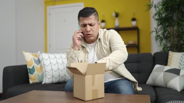 若いヒスパニック系の男が家で段ボール箱を開梱電話で話している — ストック動画