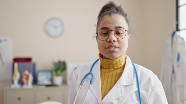Joven Afroamericana Mujer Médico Sonriendo Confiado Pie Clínica — Vídeos de Stock