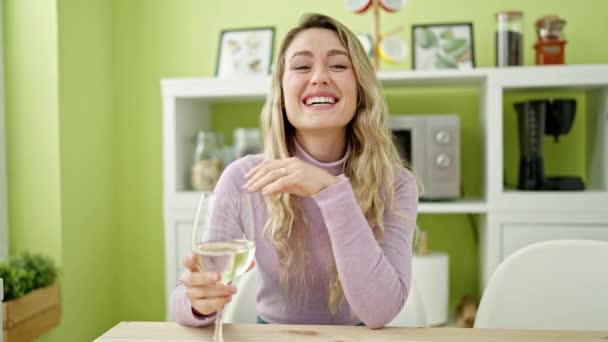 若いですブロンド女性飲むガラスのワイン座っています上のテーブルの上で話すダイニングルーム — ストック動画