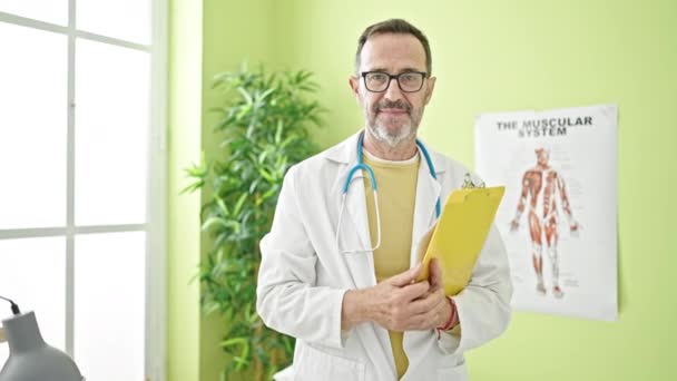 Lekarz Średnim Wieku Uśmiechający Się Pewnie Trzymając Notatnik Klinice — Wideo stockowe