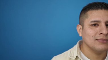 İzole edilmiş mavi arka planda duran kendine güvenen İspanyol genç adam.