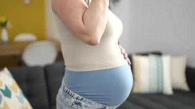 Genç hamile kadın bir bardak su içip karnına dokunuyor.