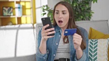 Genç, güzel, İspanyol bir kadın akıllı telefon ve kredi kartıyla alışveriş yapıyor.