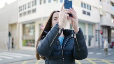 Beyaz bir kadın gülümsüyor. Akıllı telefonuyla caddede kendine güvenen bir video kaydı yapıyor.