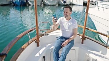 Orta yaşlı bir adam limanda teknede video görüşmesi yapıyor.