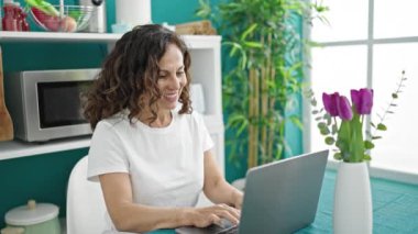 Orta yaşlı İspanyol kadın yemek odasında laptopunu masada otururken kazanan yüz ifadesiyle oturuyor.