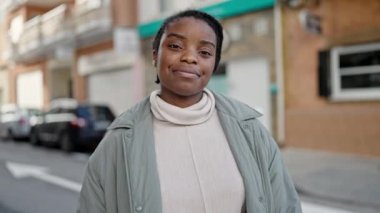 Afro-Amerikalı kadın, rahat bir ifadeyle ve kollarını kavuşturarak caddede duruyor.