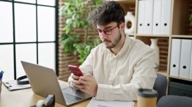 Ofiste dizüstü bilgisayar ve akıllı telefon kullanan İspanyol bir iş adamı.