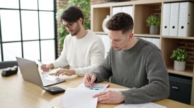 Ofiste çalışan iki erkek iş ortağı dizüstü bilgisayarda yazı yazıyor.