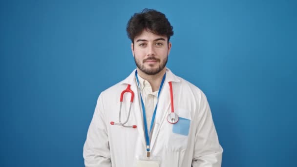 年轻的惊慌失措的医生面带微笑 自信地站在孤独的蓝色背景之上 — 图库视频影像