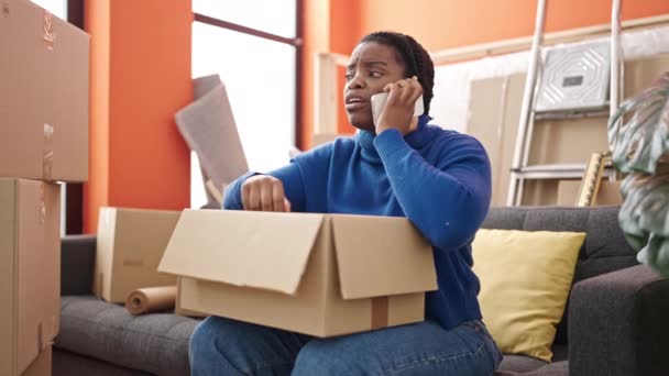 Afrykańska Amerykanka Rozmawia Przez Telefon Rozpakowując Kartonowe Pudełko Nowym Domu — Wideo stockowe