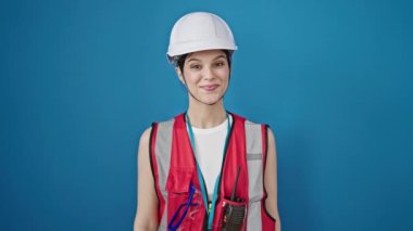 Miğfer ve mavi yelek giyen genç kadın mühendis beyaz arka planda izole edilmiş. Sert bir gülümsemesi olan kadın model.