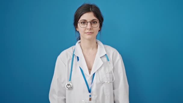 青い背景に白いコートとスタスコープを持つ美しい若い女性医師のクローズアップポートレート — ストック動画
