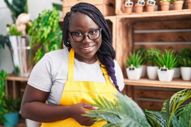 Afrikalı Amerikalı kadın çiçekçi çiçekçiye dokunduğundan emin bir şekilde gülümsüyor.