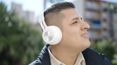 Genç İspanyol adam parkta müzik dinliyor.