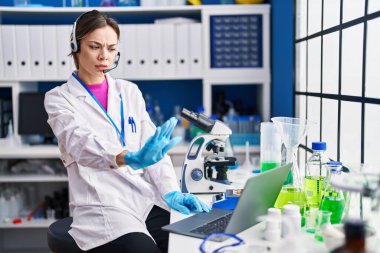 İspanyol kadın, laboratuvarda çalışıyor. Açık elle, dur işareti yapıyor. Ciddi ve kendinden emin bir ifadeyle. 