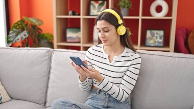 Genç, güzel, İspanyol bir kadın evdeki kanepede oturmuş müzik dinliyor.