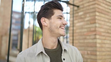 Young hispanic man smiling confident looking to the side at street