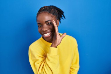 Güzel siyahi kadın mavi arka planda el ele durur gizli dedikodular anlatır, kötü niyetli konuşmalar fısıldar. 