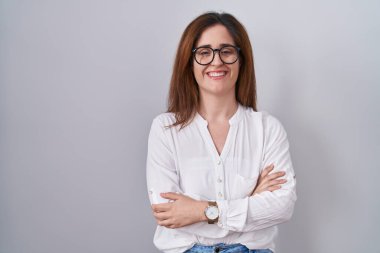 Esmer kadın, izole edilmiş beyaz arka planda durup kollarını kavuşturup kameraya bakarken gülümseyen mutlu bir yüz. pozitif kişi. 
