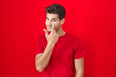 Genç İspanyol bir adam kırmızı arka planda dikiliyor. Göze bakıyor. Senin jestini izliyor. 