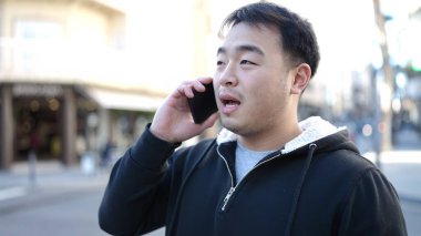 Young chinese man talking on smartphone with serious expression at street