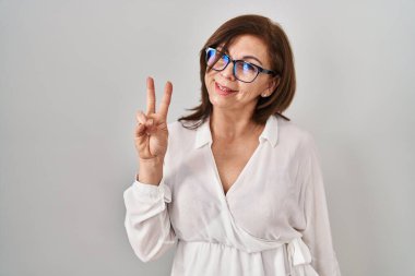 Orta yaşlı İspanyol kadın izole edilmiş arka planda duruyor. İki numarayı işaret ediyor ve gülümsüyor. Kendinden emin ve mutlu.. 