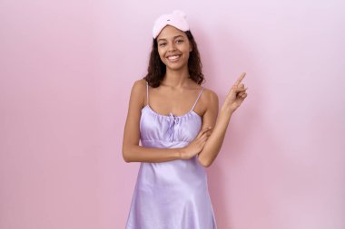 Genç İspanyol kadın uyku maskesi takıyor ve yüzünde kocaman bir gülümseme olan gecelikle, kameraya el ile işaret ediyor.. 