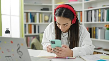 Genç, güzel İspanyol kız öğrenci üniversite sınıfında akıllı telefon kullanarak notlar yazıyor.