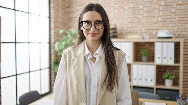 Genç, güzel, İspanyol bir iş kadını ofiste kendinden emin gülümsüyor.